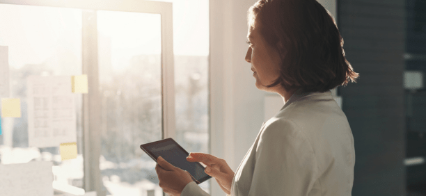 Woman holding a tablet looking out a window.