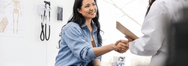 Young woman smiles and shakes hands with her doctor. 
