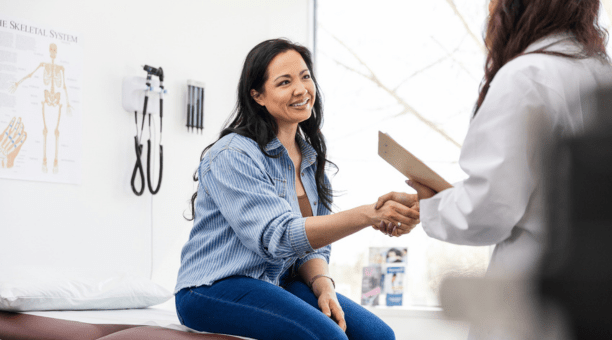 Young woman smiles and shakes hands with her doctor. 