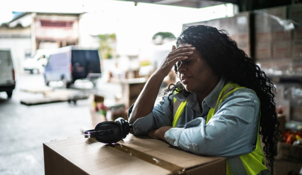 Stressed warehouse worker with her hands to her forehead.