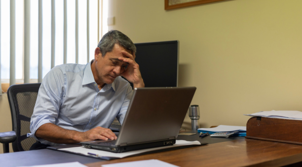 Minority man at work looking depressed while sitting at his desk on a laptop.