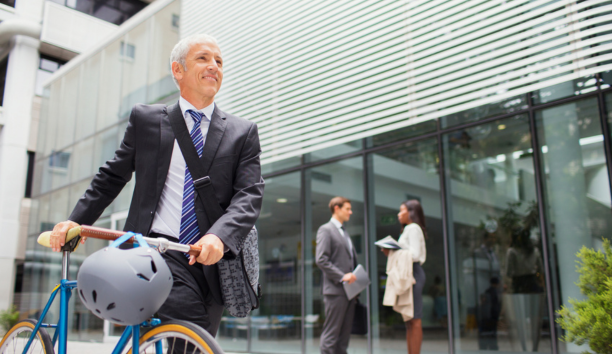Man bikes to work with other professionals behind him in front of office building. 