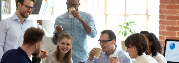 Diverse group of coworkers drinking coffee and laughing while working at a conference table. 