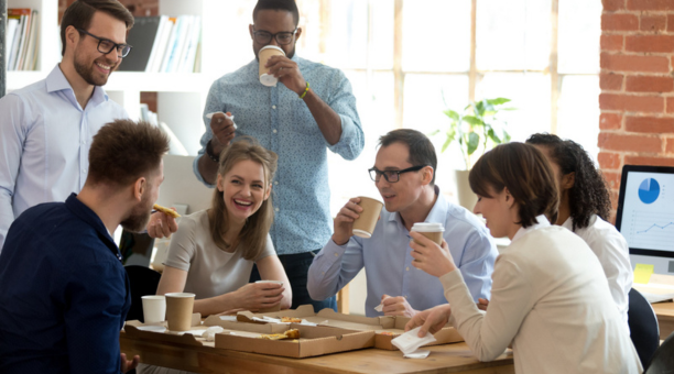 Diverse group of coworkers drinking coffee and laughing while working at a conference table. 
