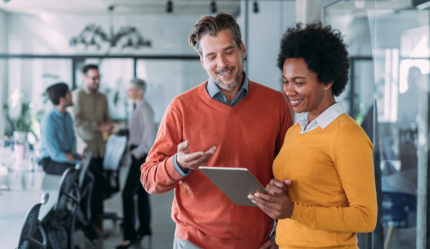 Man and woman looking at tablet in office smiling. 