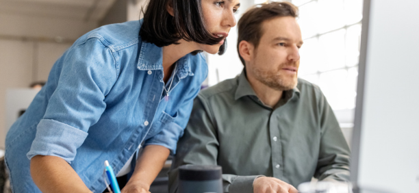 Male and female employees looking at a computer together. 
