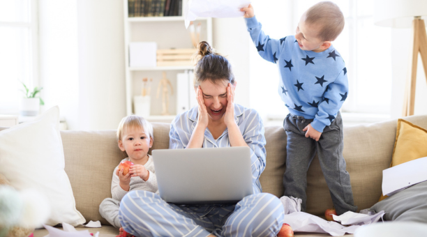 Stressed mom sitting on couch with two kids and an open laptop.