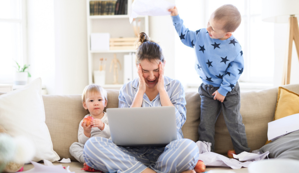 Stressed mom sitting on couch with two kids and an open laptop.