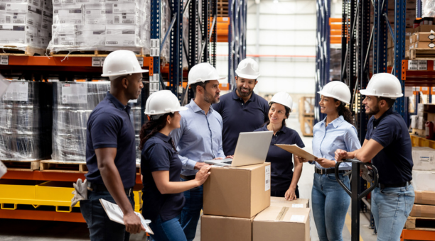Group of employees wearing hard hats talking in a warehouse. 